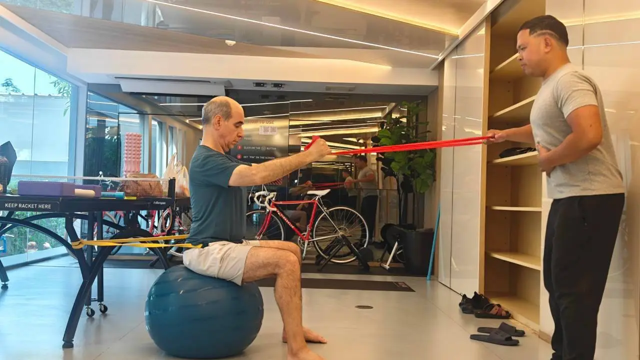Client doing a resistance band shoulder pull on a stability ball while Boss checks form