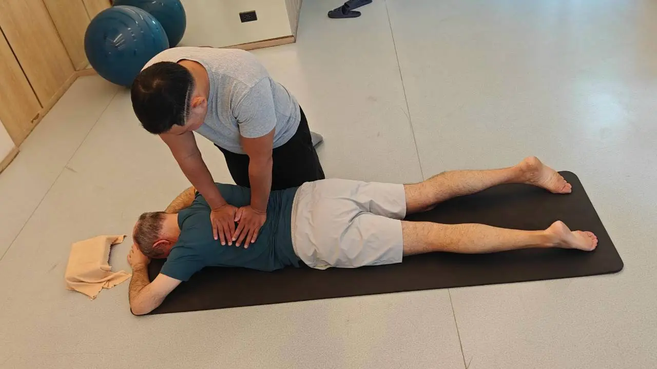 Boss assessing a client's lower back with gentle hands-on pressure on a mat