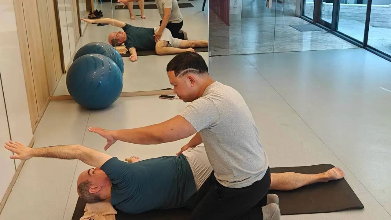 Boss guiding a client through a gentle shoulder mobility reach on a mat