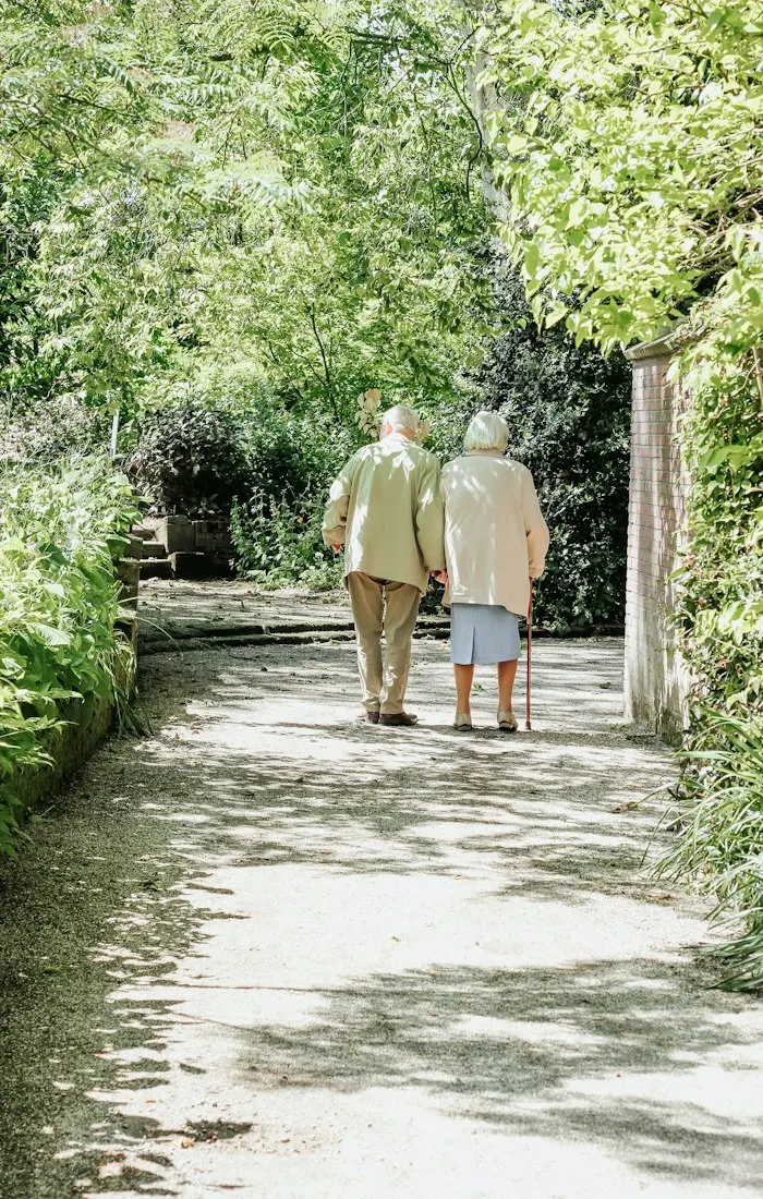 Older couple walking together along a leafy garden path