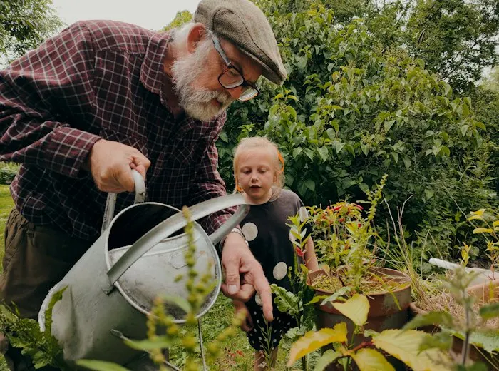 Grandfather watering plants with his grandchild