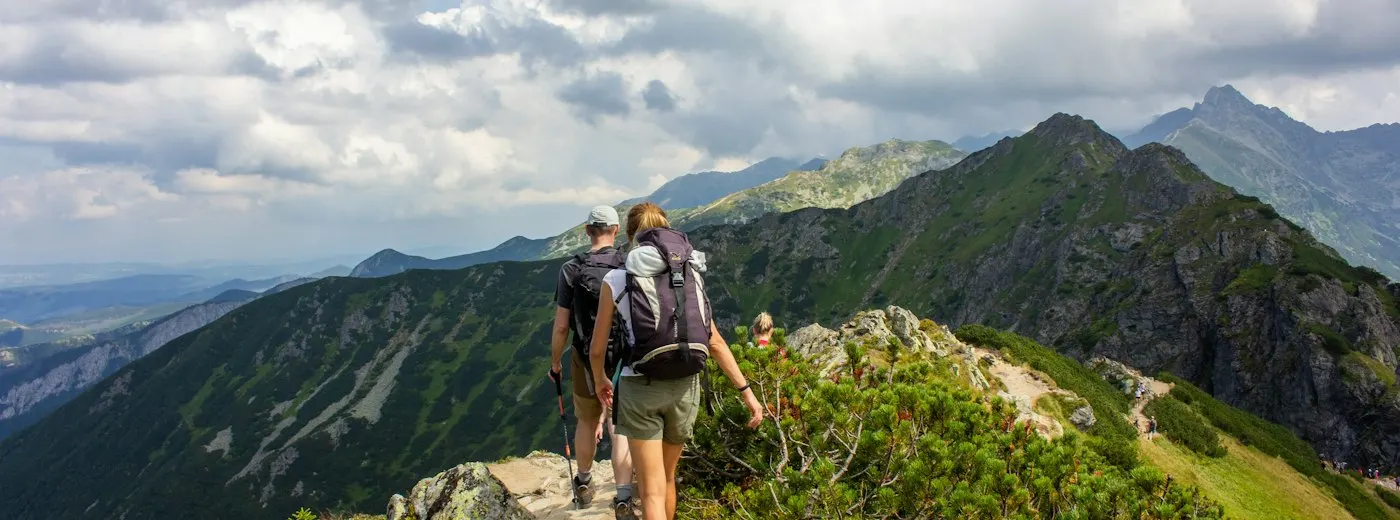 Two hikers walking a mountain ridge under a cloudy sky
