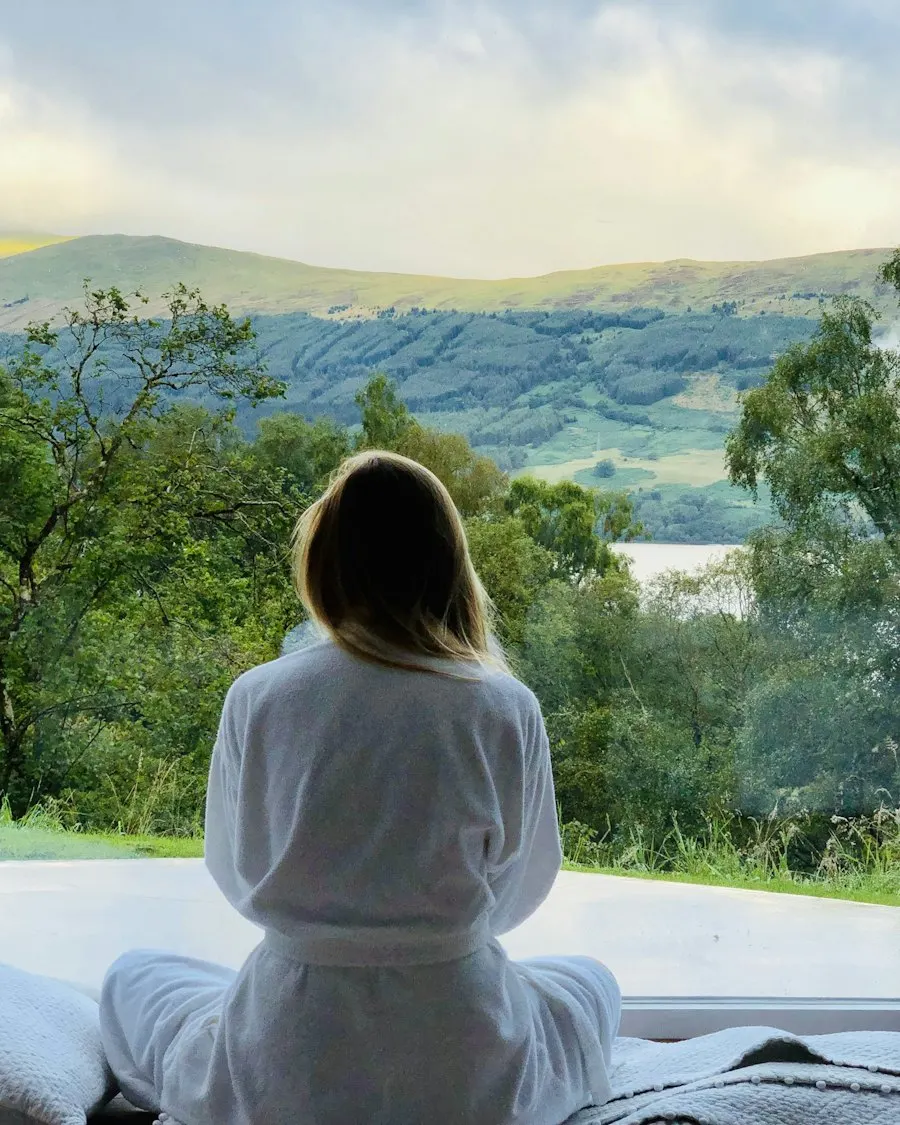 Woman in a white robe looking over green hills from a villa terrace